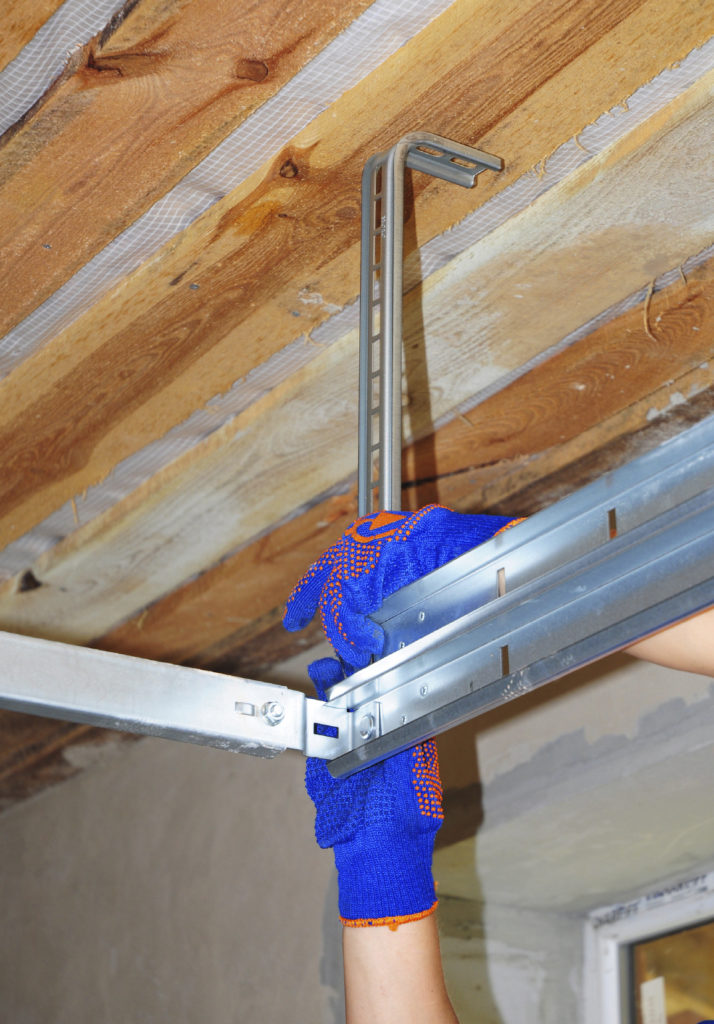 Contractor Installing Garage Door Metal Profil  Post Rail and Spring Installation and Garage Ceiling.  Spring Tension Lifts Section Garage Door Panel that  Motor does not have to Lift Entire Weight.